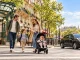 Famille avec deux enfants, dont un en poussette, traversant un passage piéton à Paris près d’une entrée de métro, avec un taxi et la tour Eiffel en arrière-plan.
